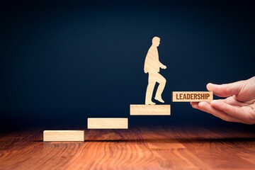 Wooden cut out of human walking up wooden steps.  The step they will step on next is labeled with the word leadership.